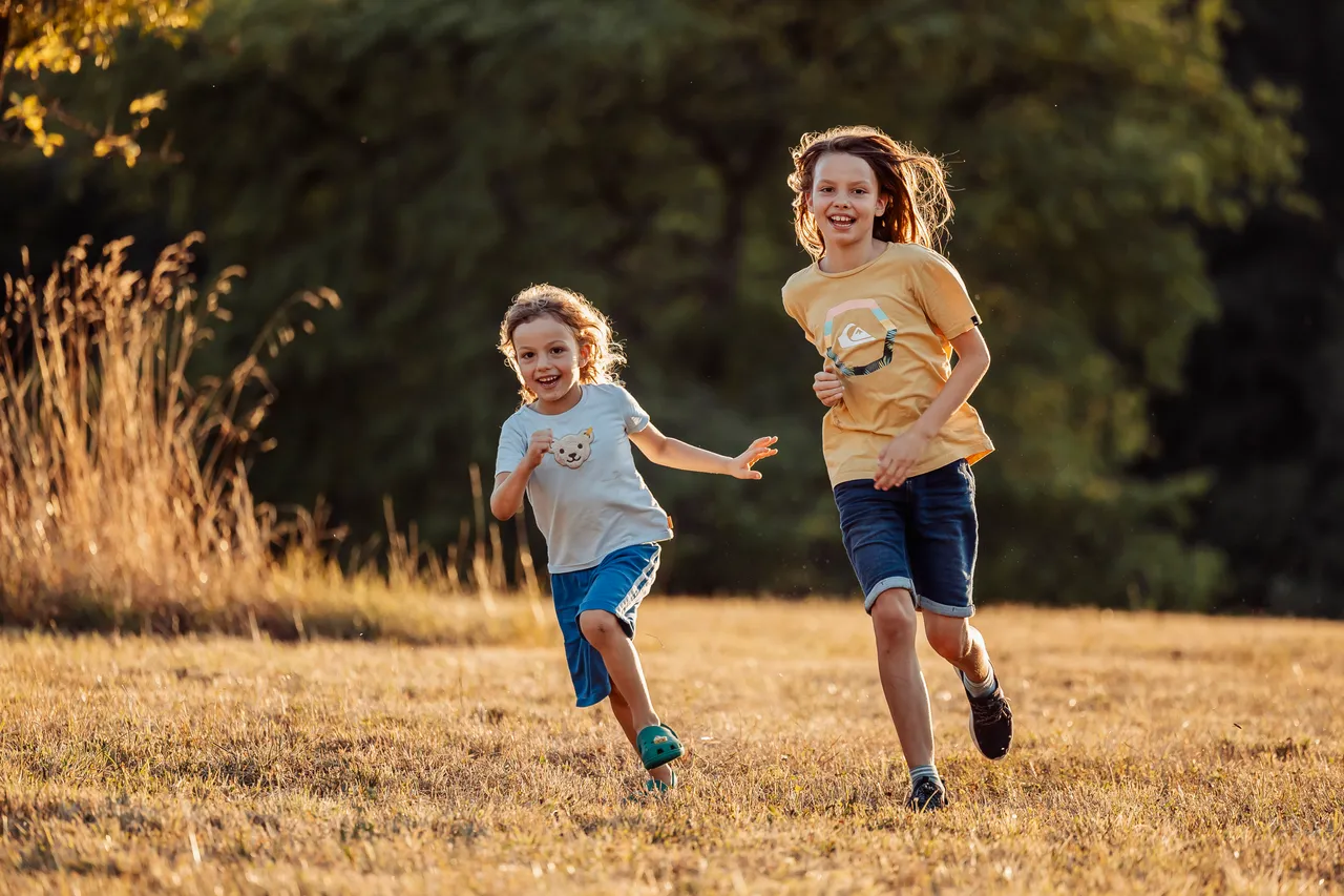 Zwei Kinder rennen lachend über eine sommerliche Wiese