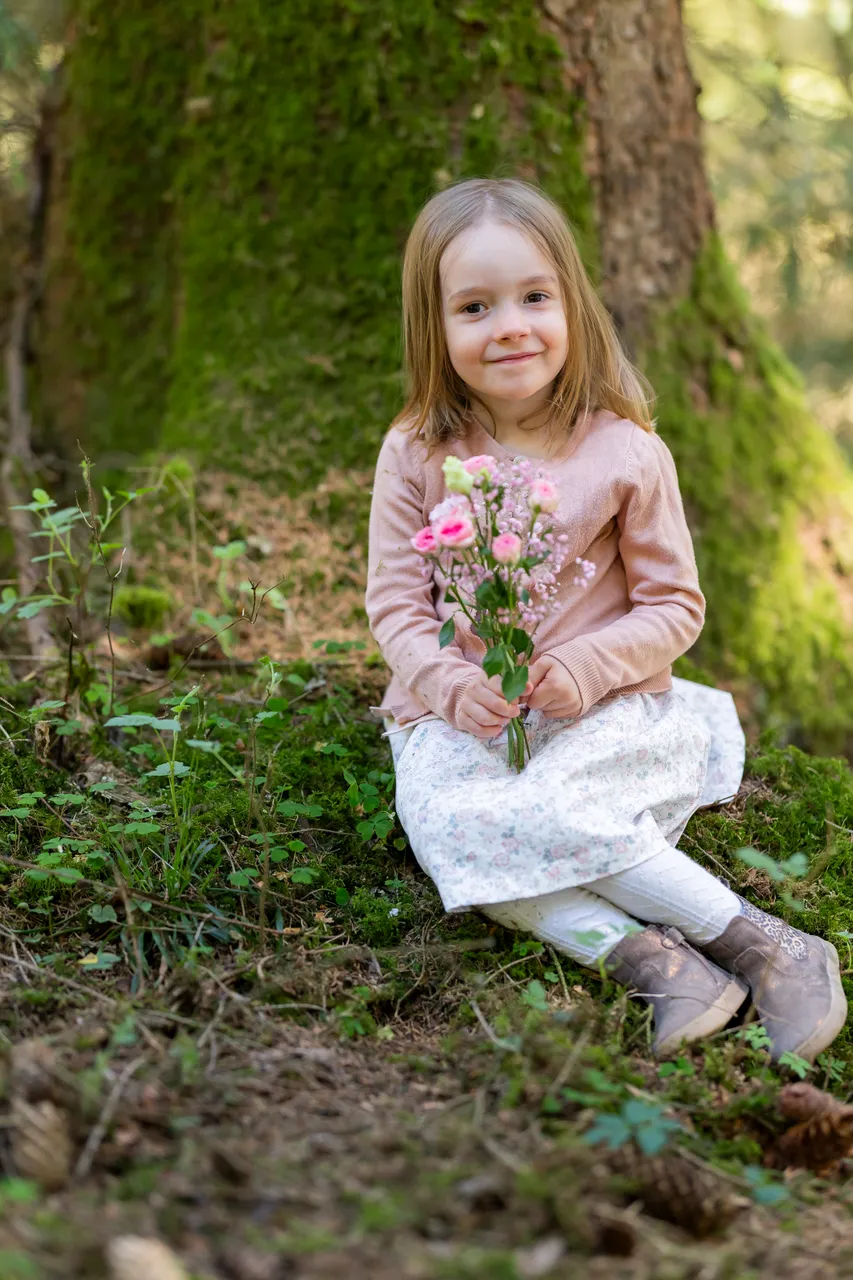 Mädchen sitzt mit einer Blume in einem grünen Wald